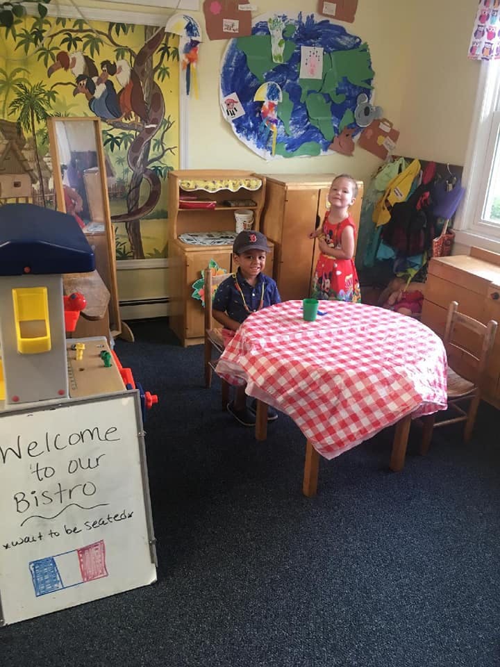 Two children in a classroom with a table covered by a red and white checkered cloth