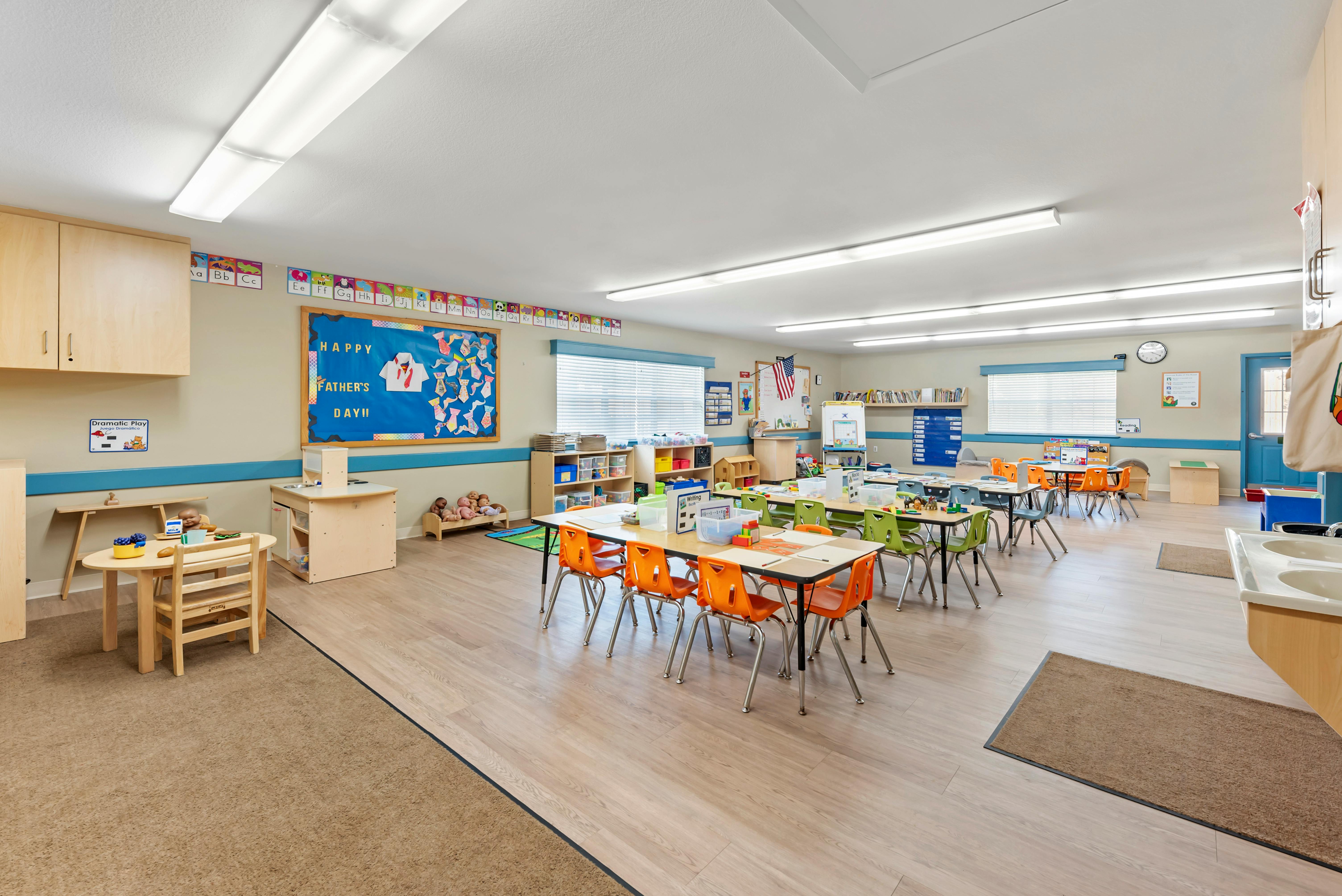Classroom with child-sized tables and chairs, bulletin board says "Happy Father's Day"