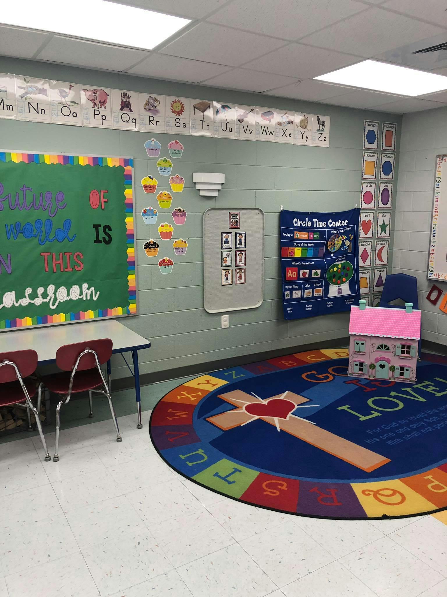 Classroom with a green bulletin board, small table, and a circular rug