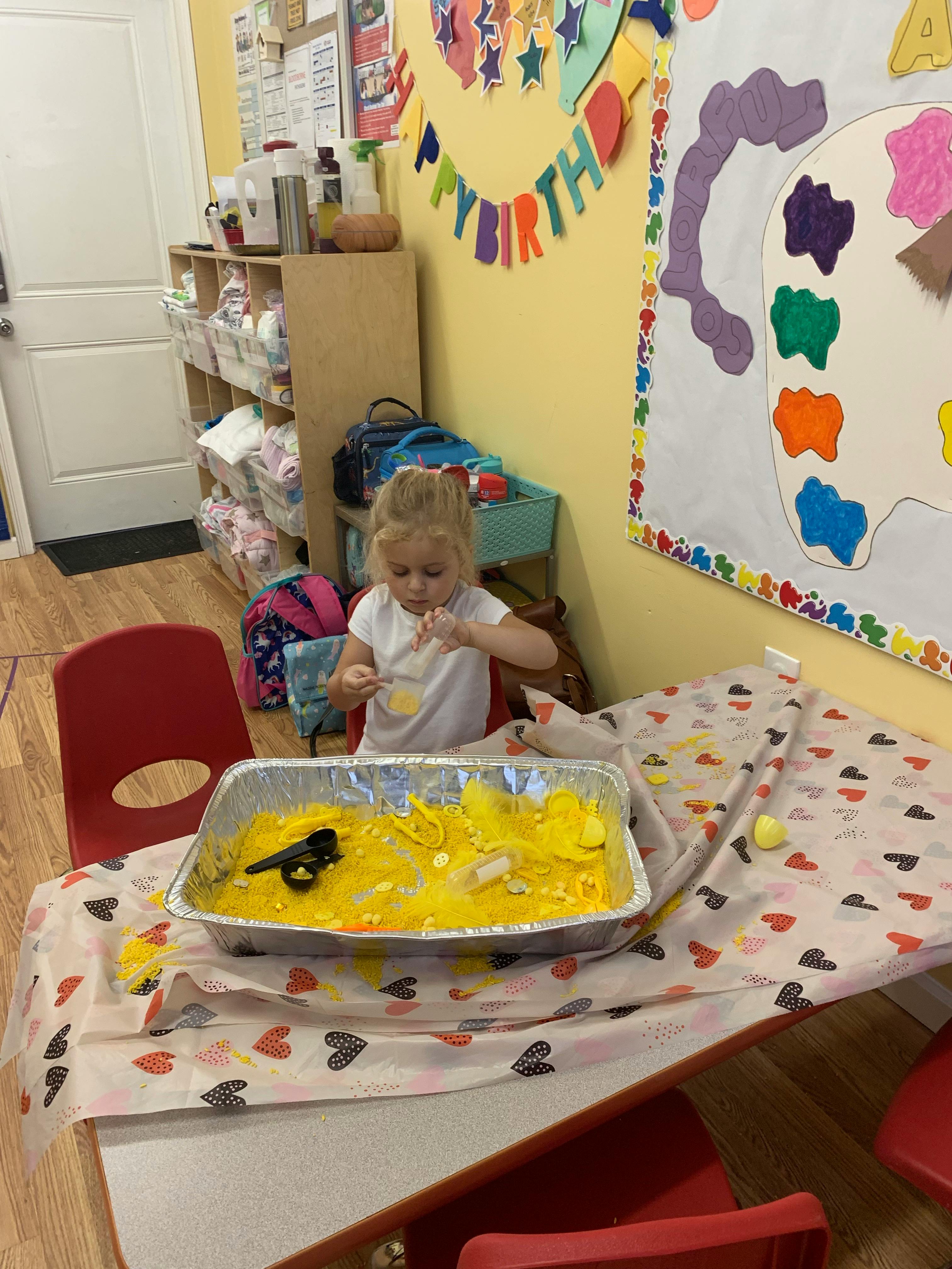 Child playing with yellow sensory bin filler at a table