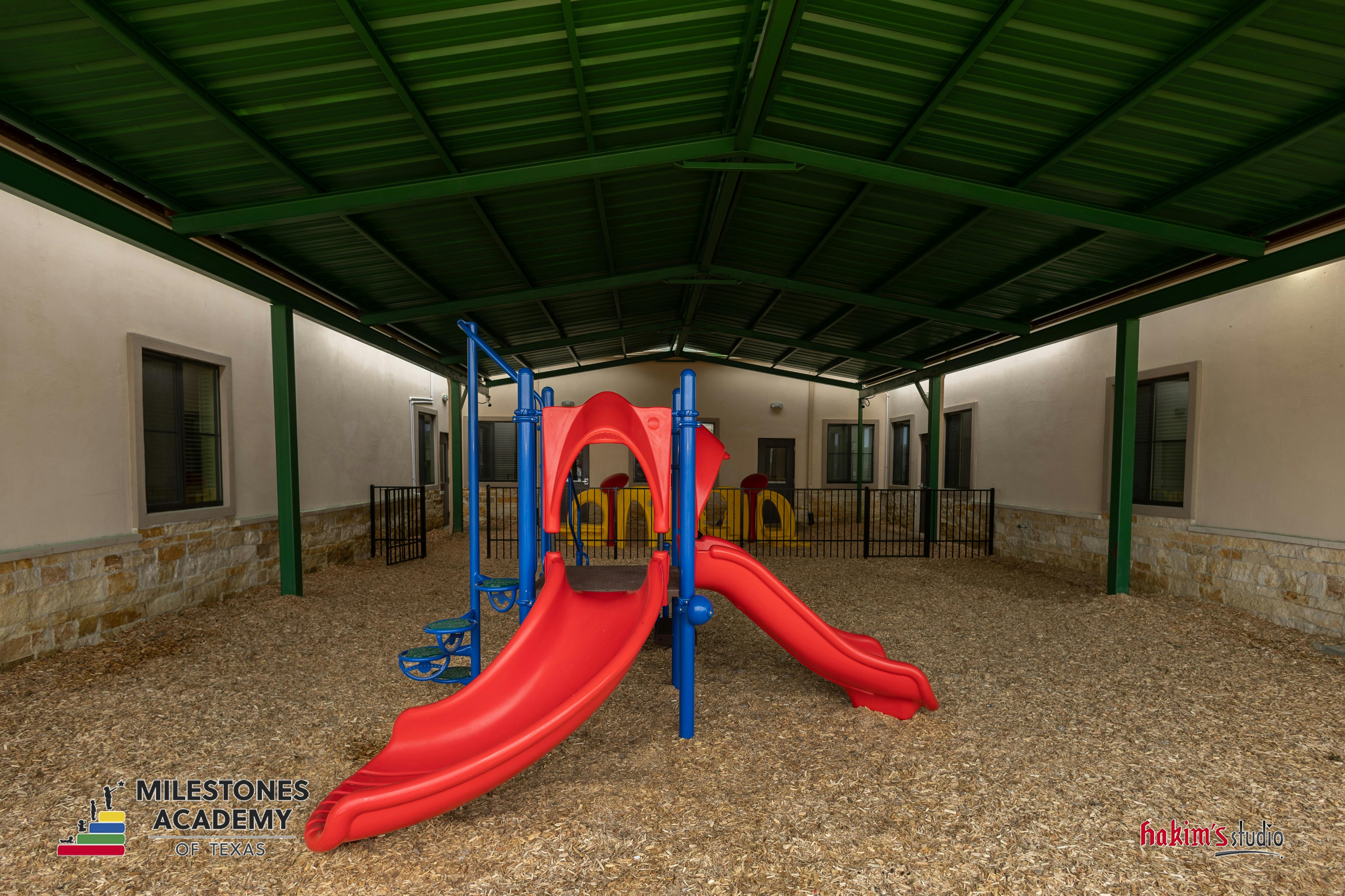 Covered outdoor playground with red and blue slides on wood chips