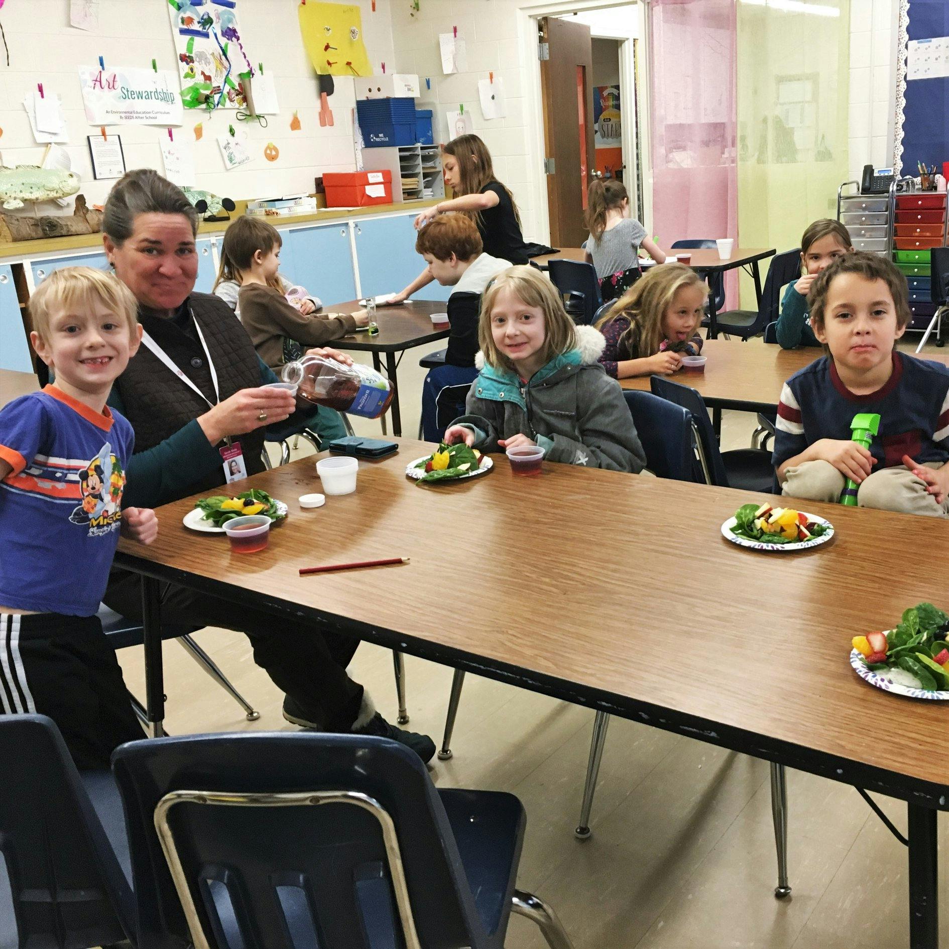 Adult and children sitting at tables with plates of food in a classroom