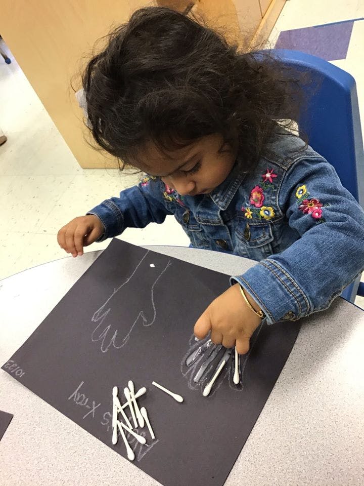 Child placing cotton swabs on a hand outline on black paper