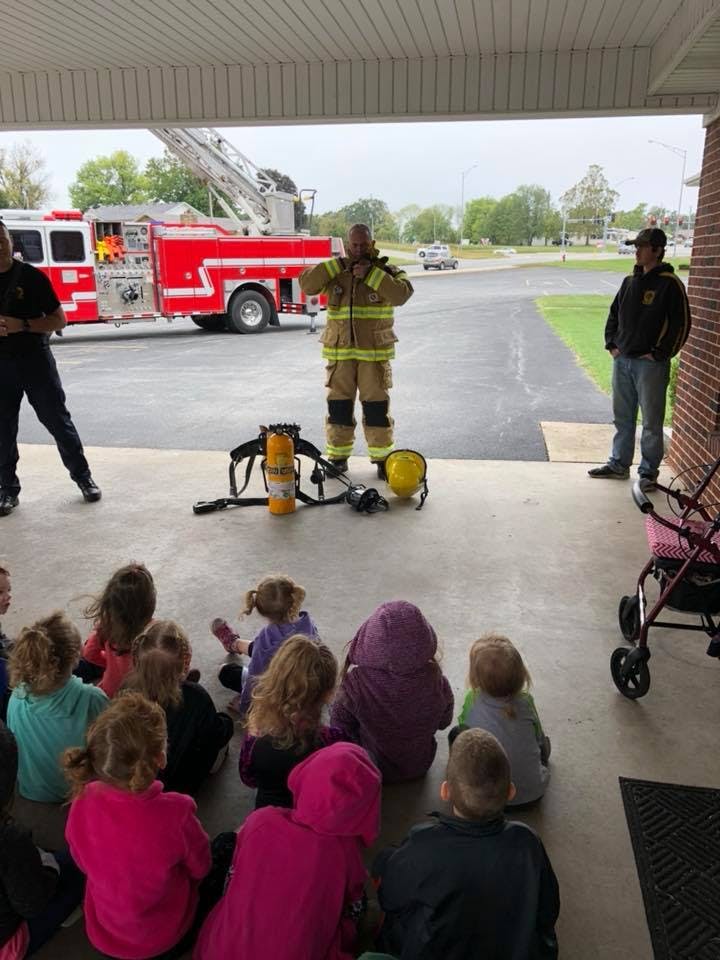 Firefighter in uniform demonstrating equipment to a group of children