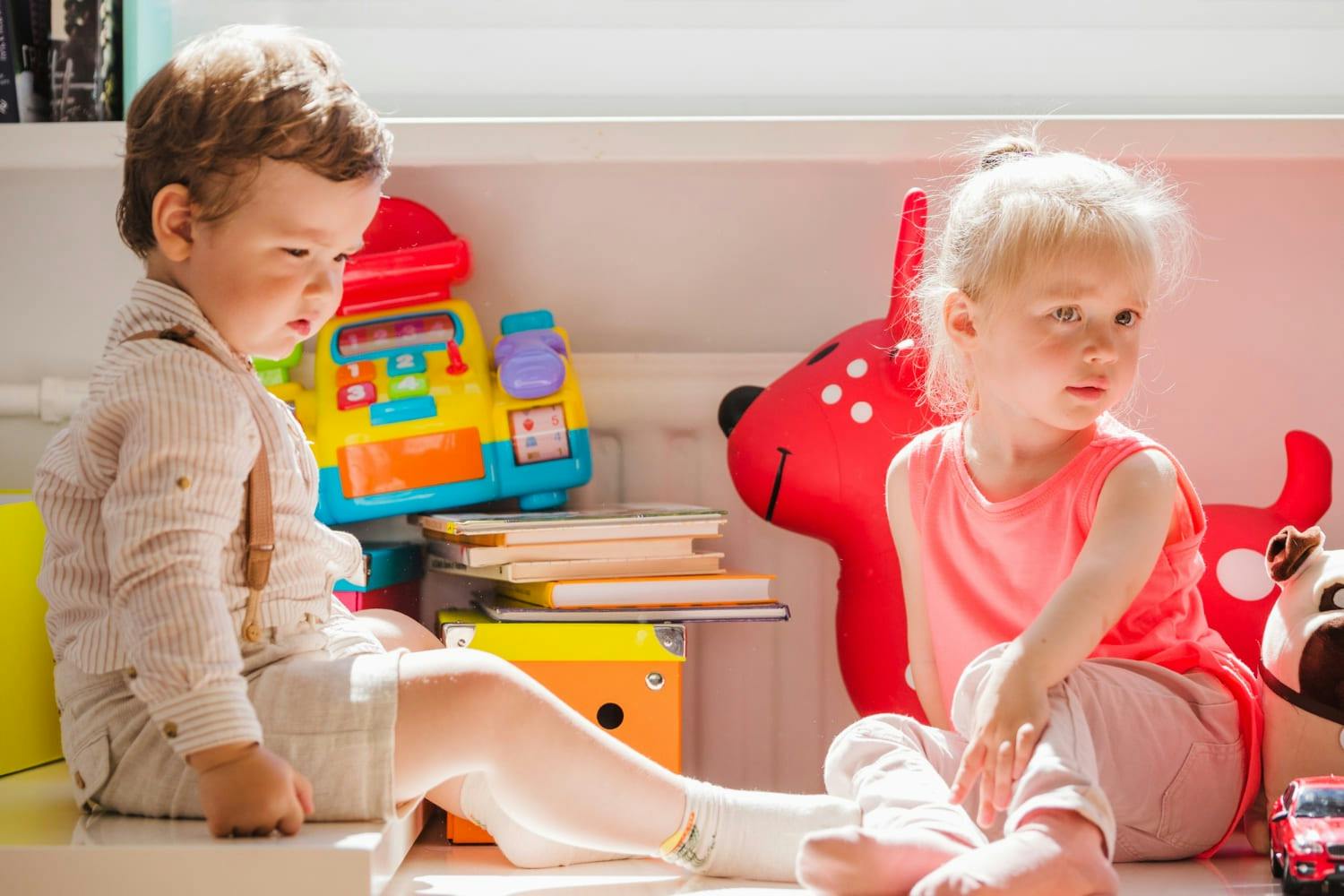 Two children sitting on the floor surrounded by toys and books