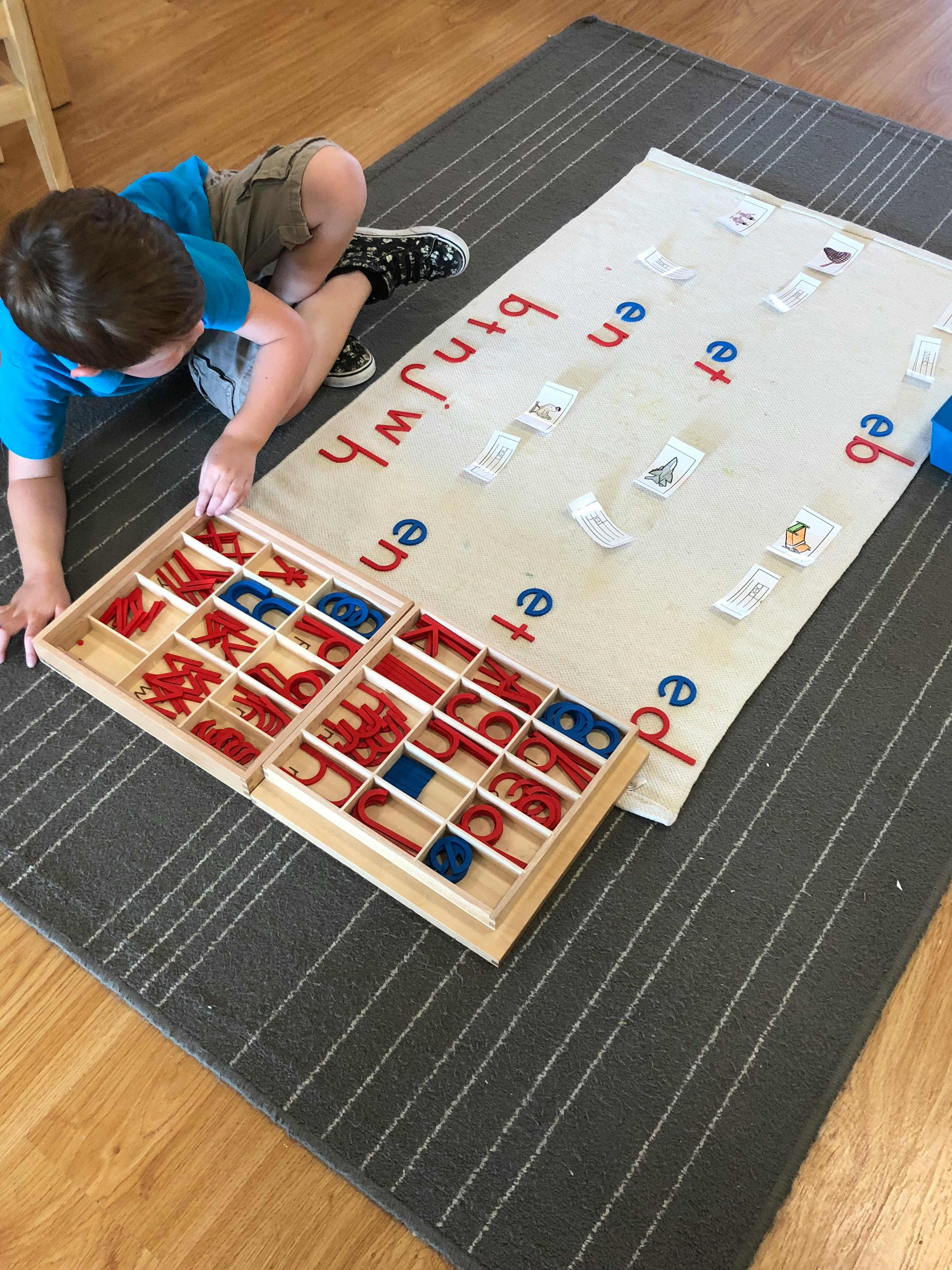 Child on floor with wooden letter tray and mat with letters