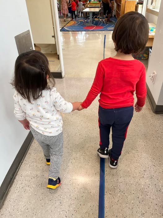 Two children holding hands and walking down a hallway