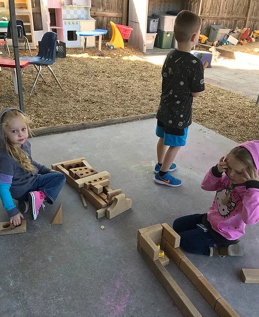 Three children playing with wooden blocks outdoors