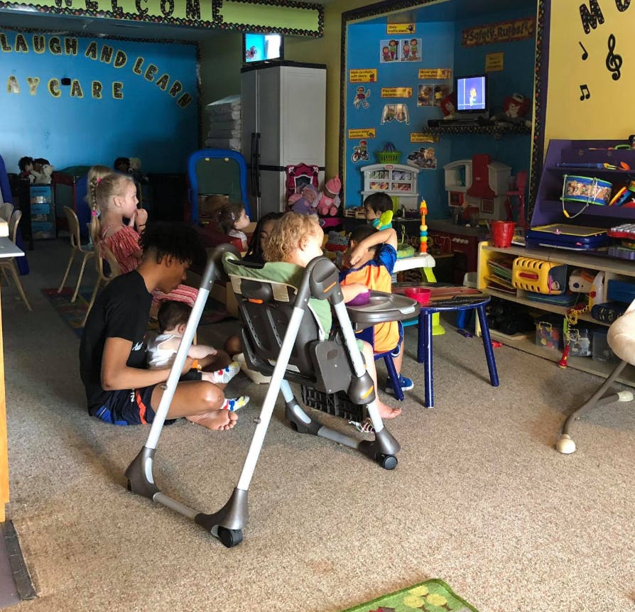 Person sitting on floor with children in high chairs in a classroom