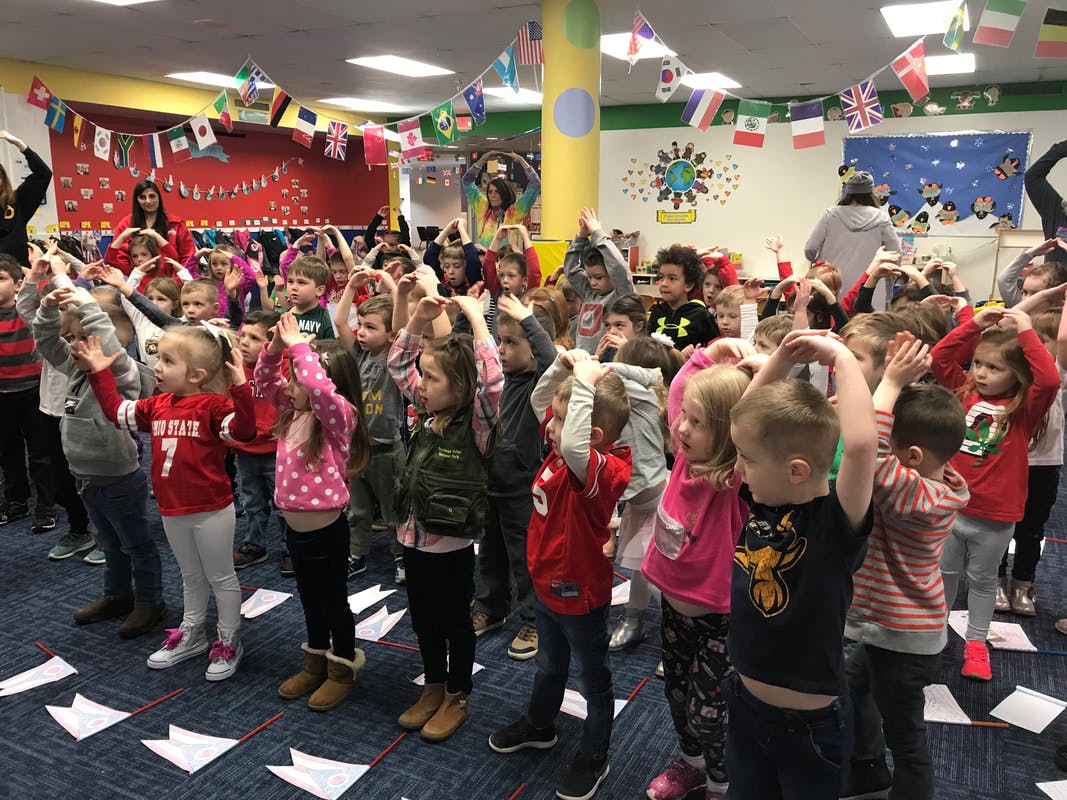 Many children standing with hands on their heads in a classroom