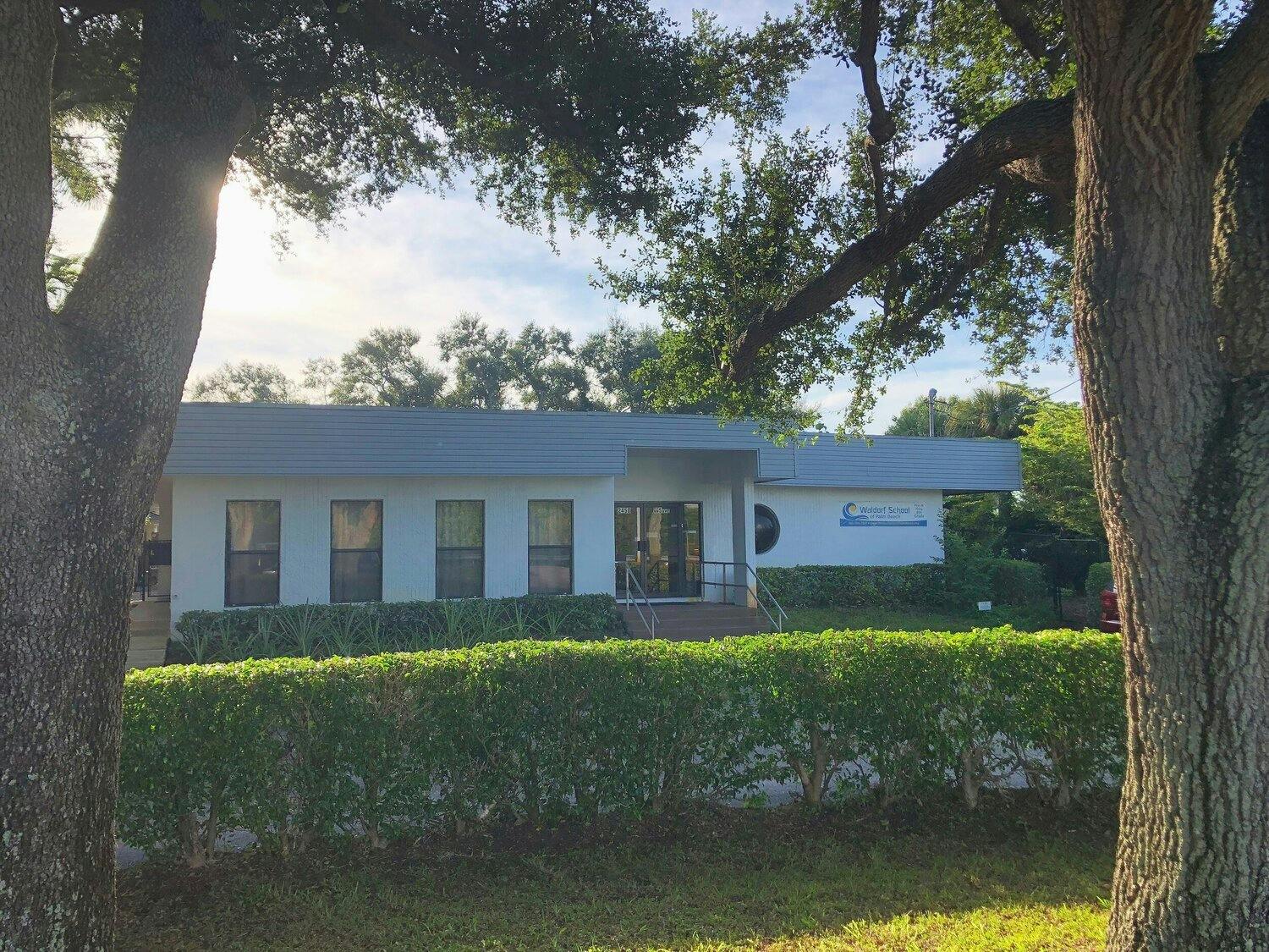 White building with a gray roof behind a green hedge