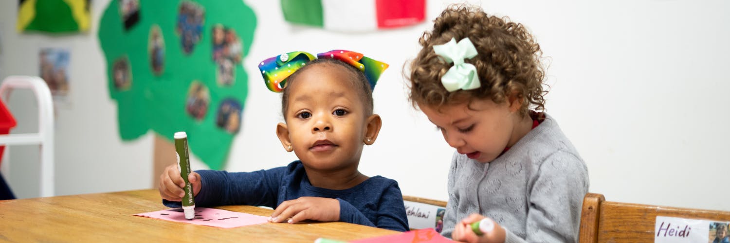 Two children drawing at a table in a classroom