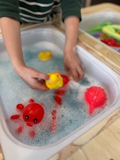 Child playing with rubber duck and toys in bubbly water