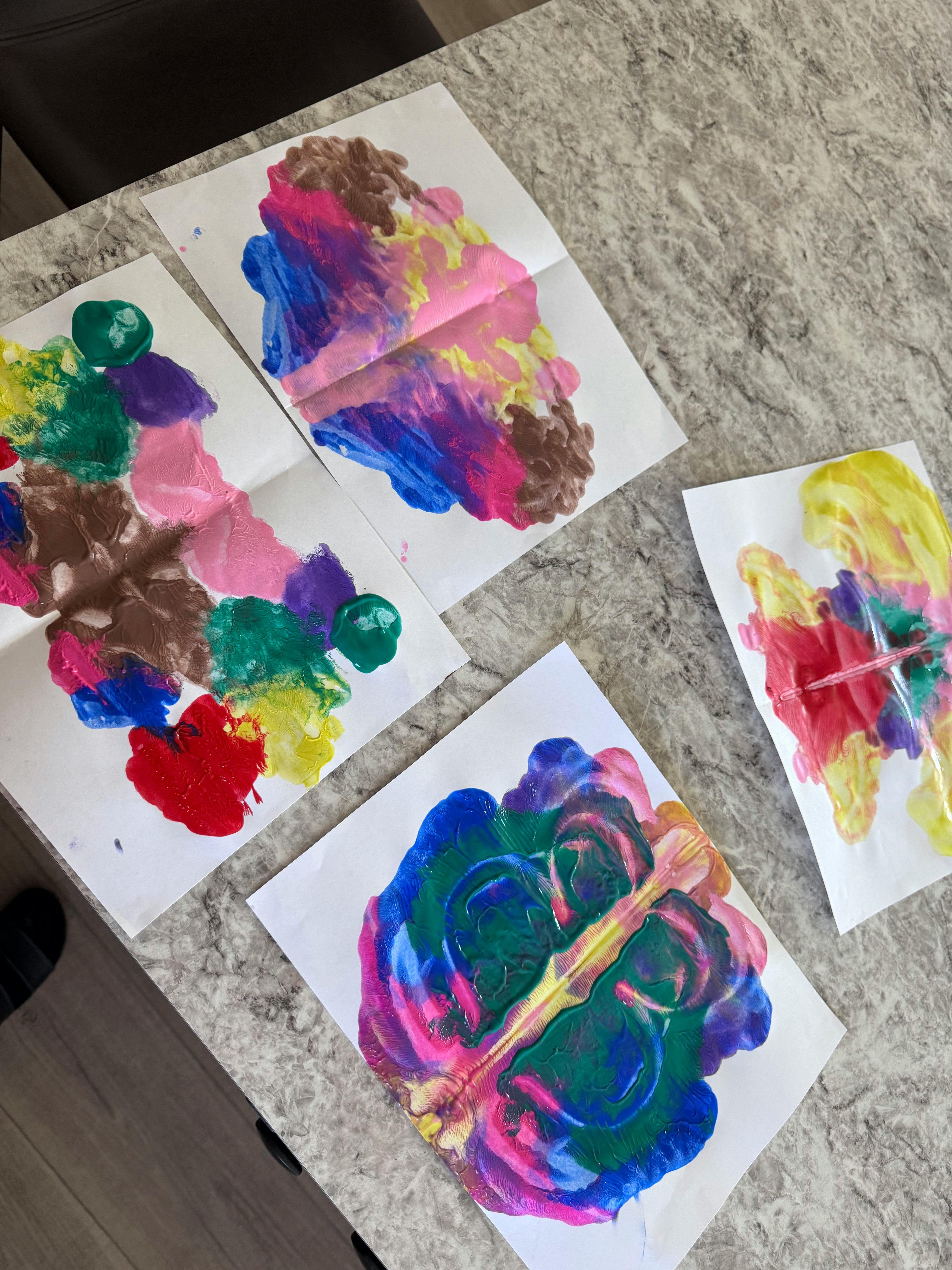 Multiple colorful paint blot art pieces on a table