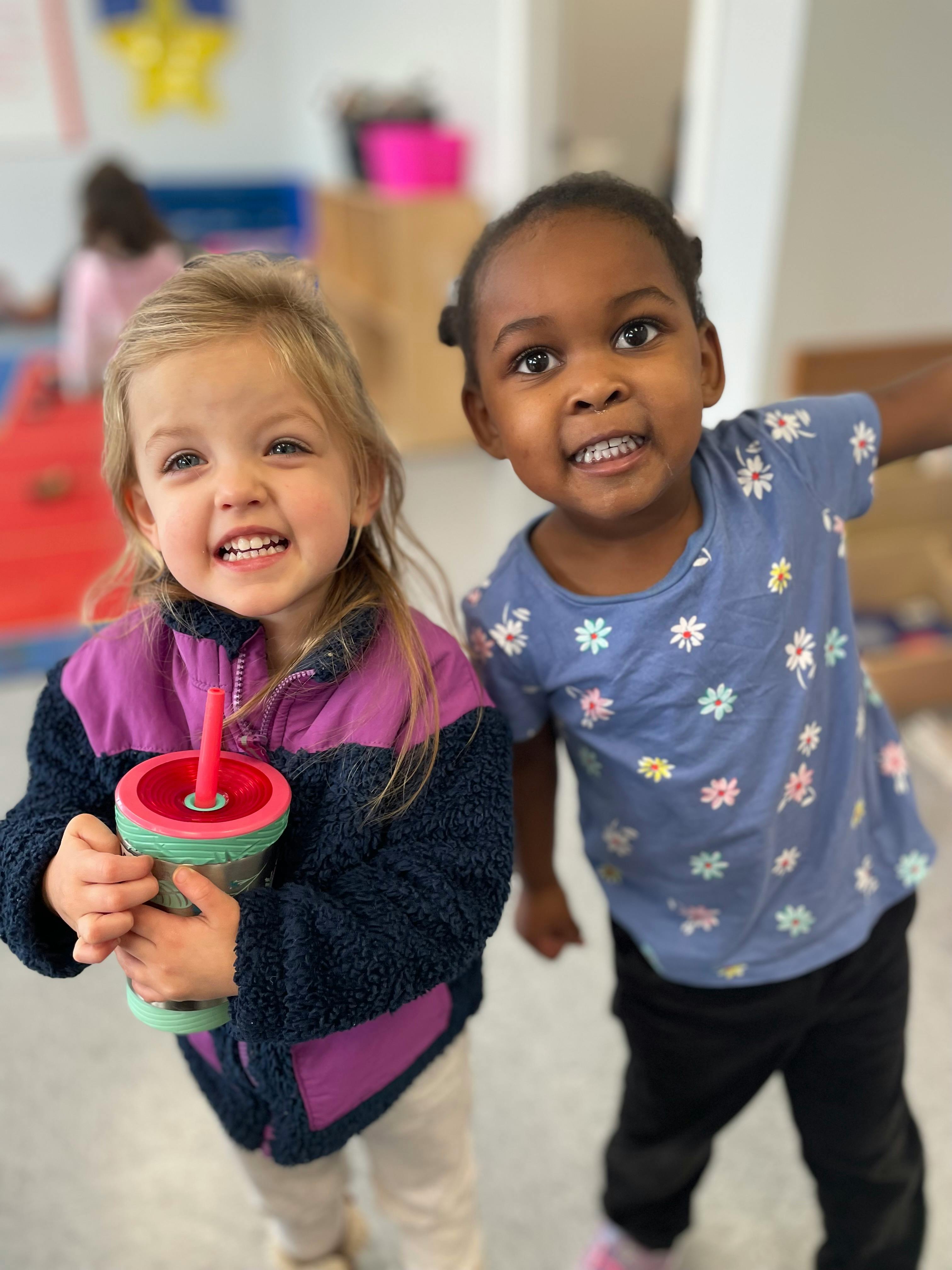Two children smiling, one holding a cup
