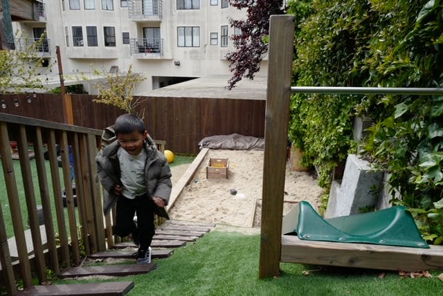 Child walking down wooden steps in a backyard with a sandbox