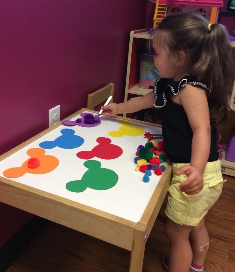 Child playing with colorful pom-poms and Mickey Mouse shapes on a table