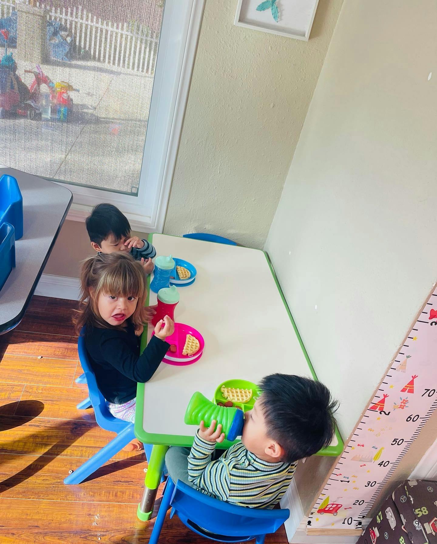 Three children sitting at a table, one drinking from a cup