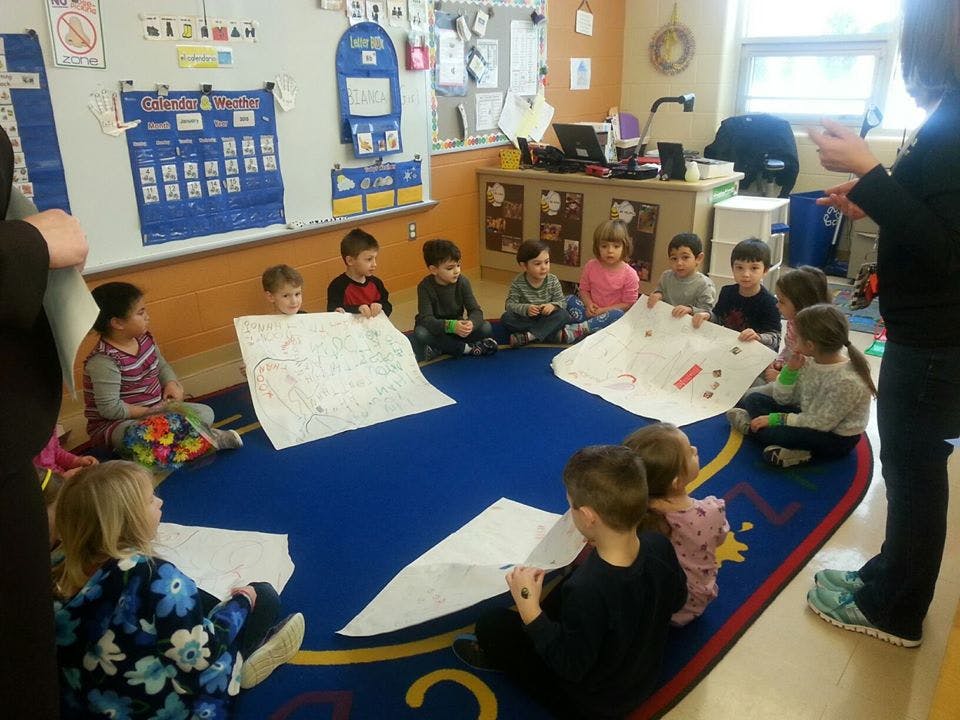 Children sitting on a rug in a classroom with papers