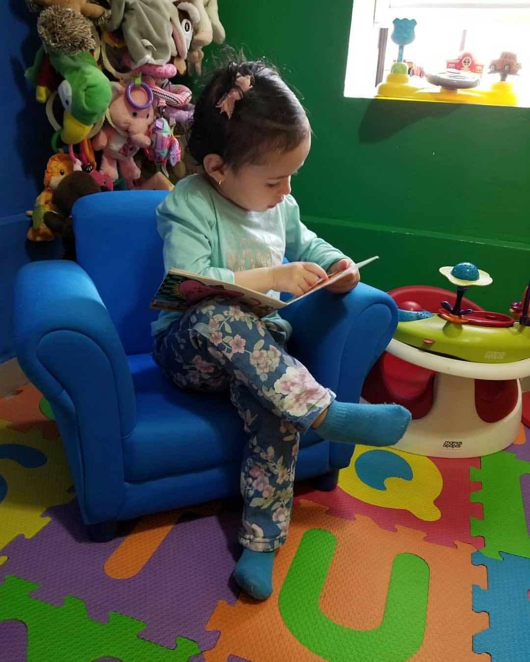 Child sitting in a blue chair reading a book