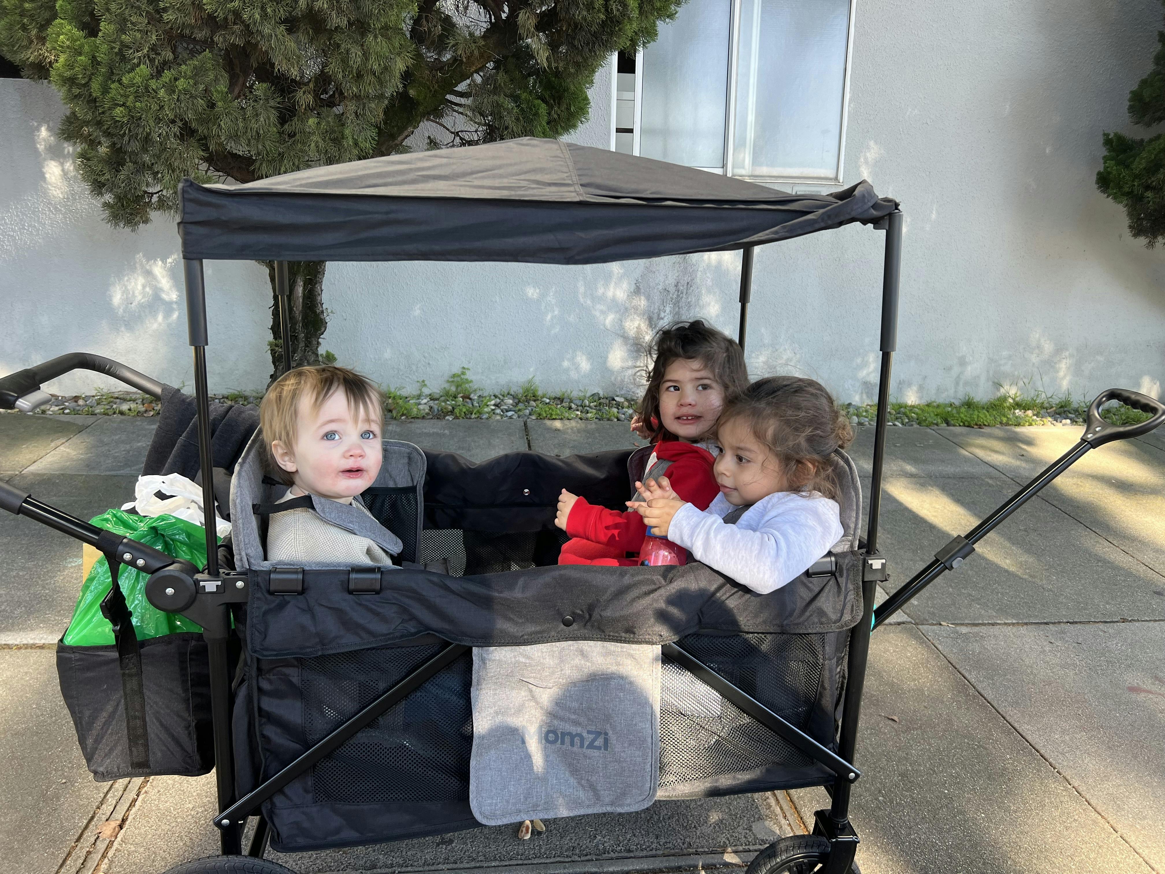 Three children in a wagon, one looking left, two looking right