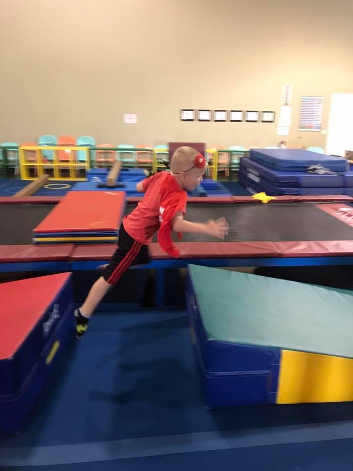 Child in red shirt jumping between two mats in a gym