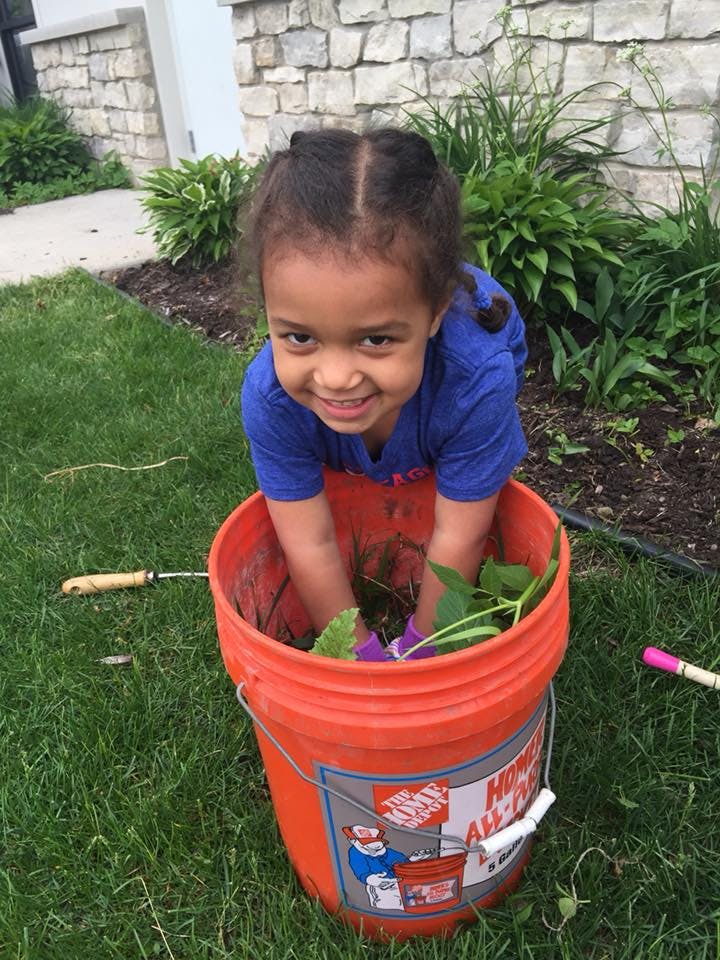 Child in an orange bucket with plants