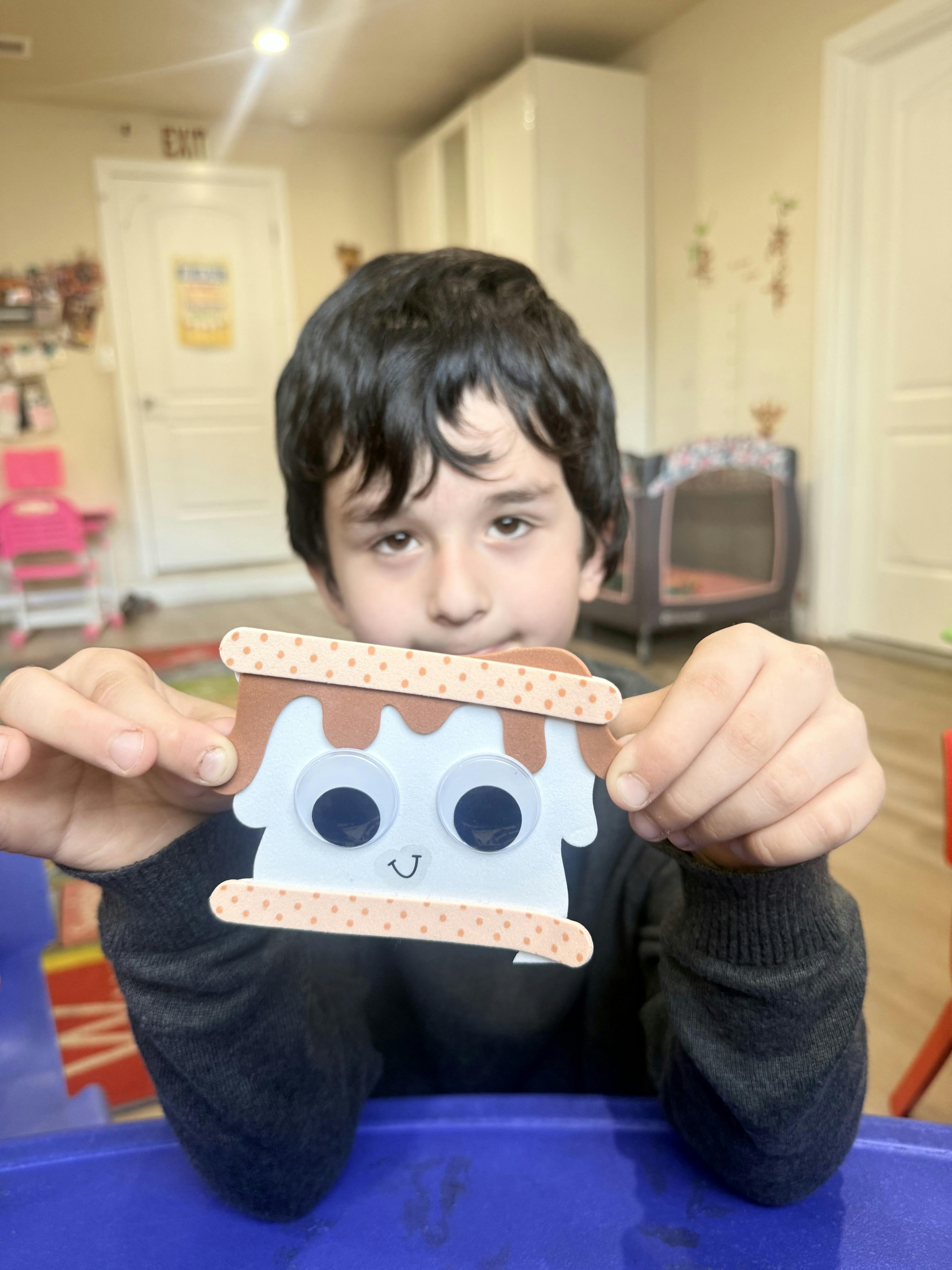 Child holding a DIY craft of a s'more with googly eyes