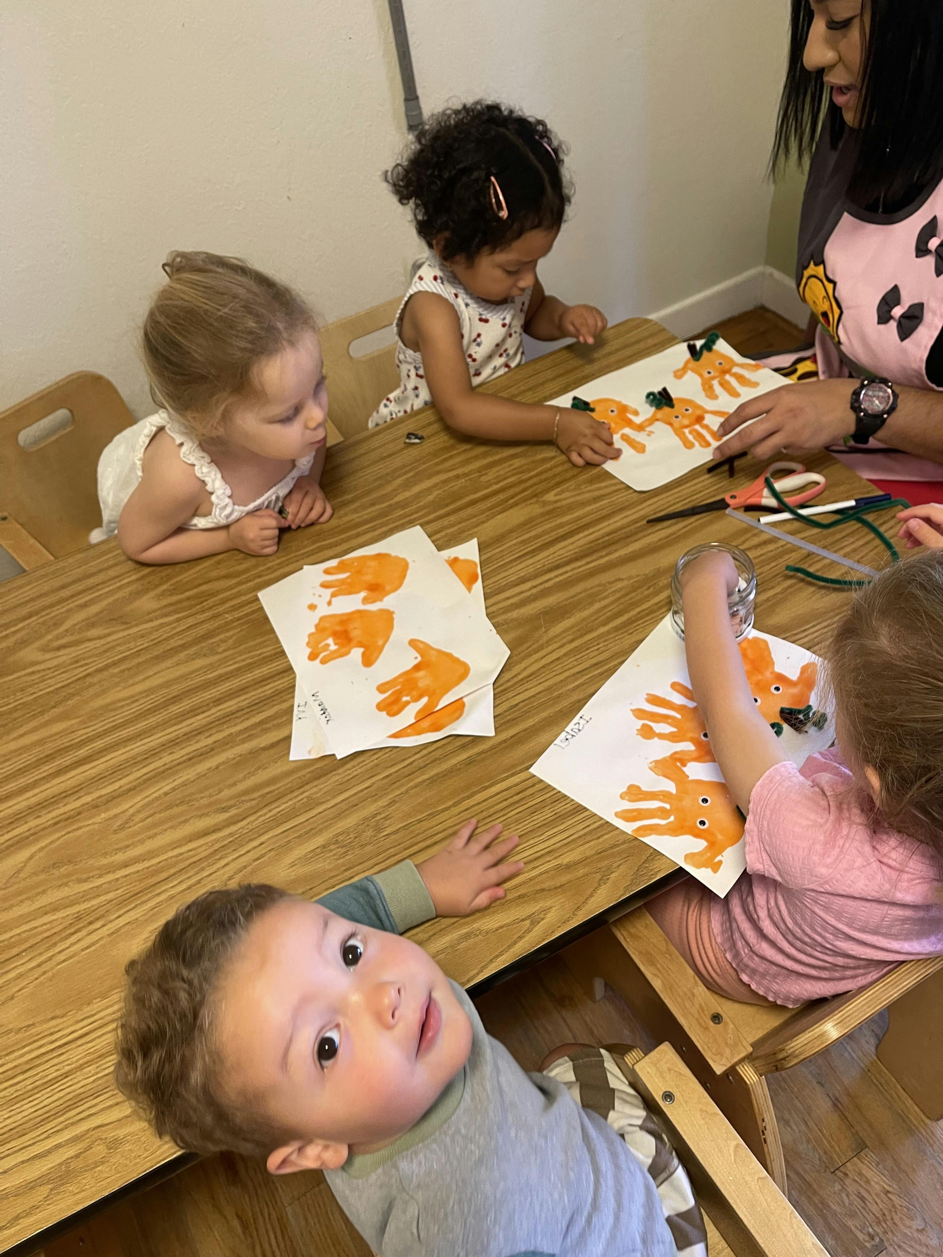 A person and children creating pumpkin handprint art at a table