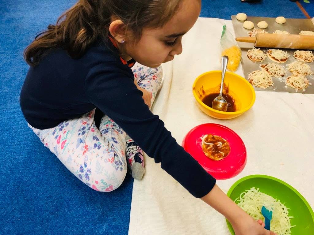 Child making mini pizzas with sauce and cheese