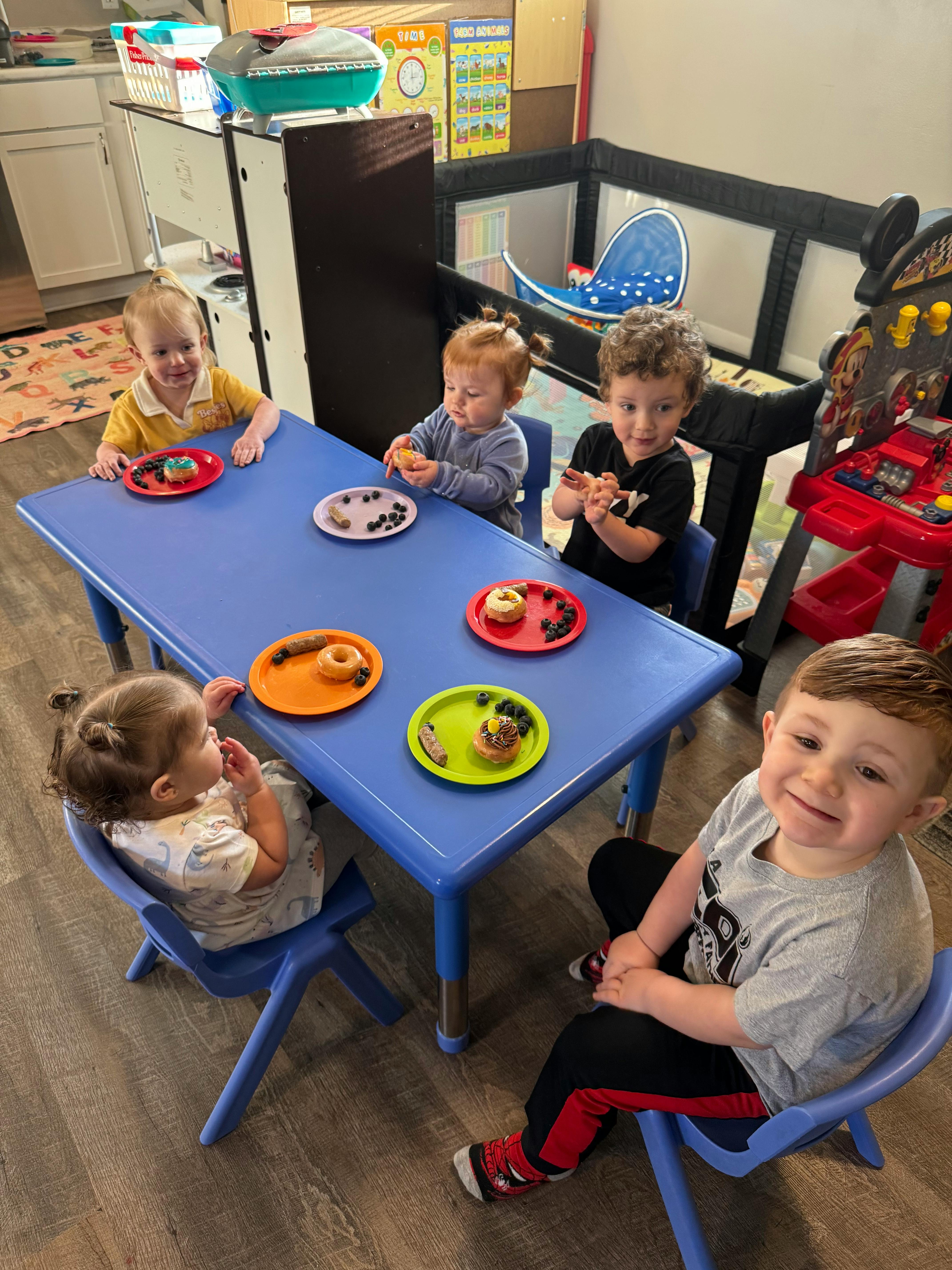 Four children sitting at a blue table with plates of snacks