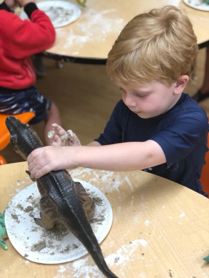 Child playing with a dinosaur toy and clay