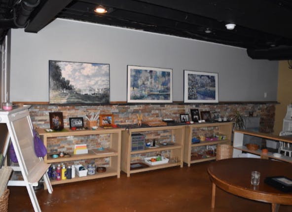 Room with shelves of items, artwork on wall, and a table