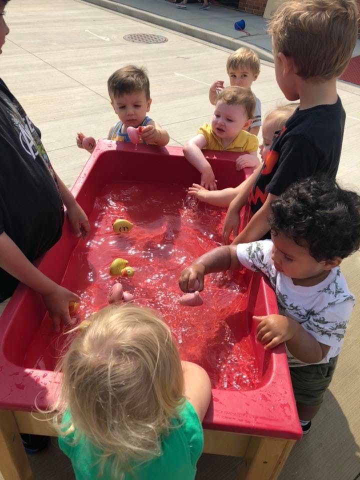Children playing with water and toys in a red sensory table