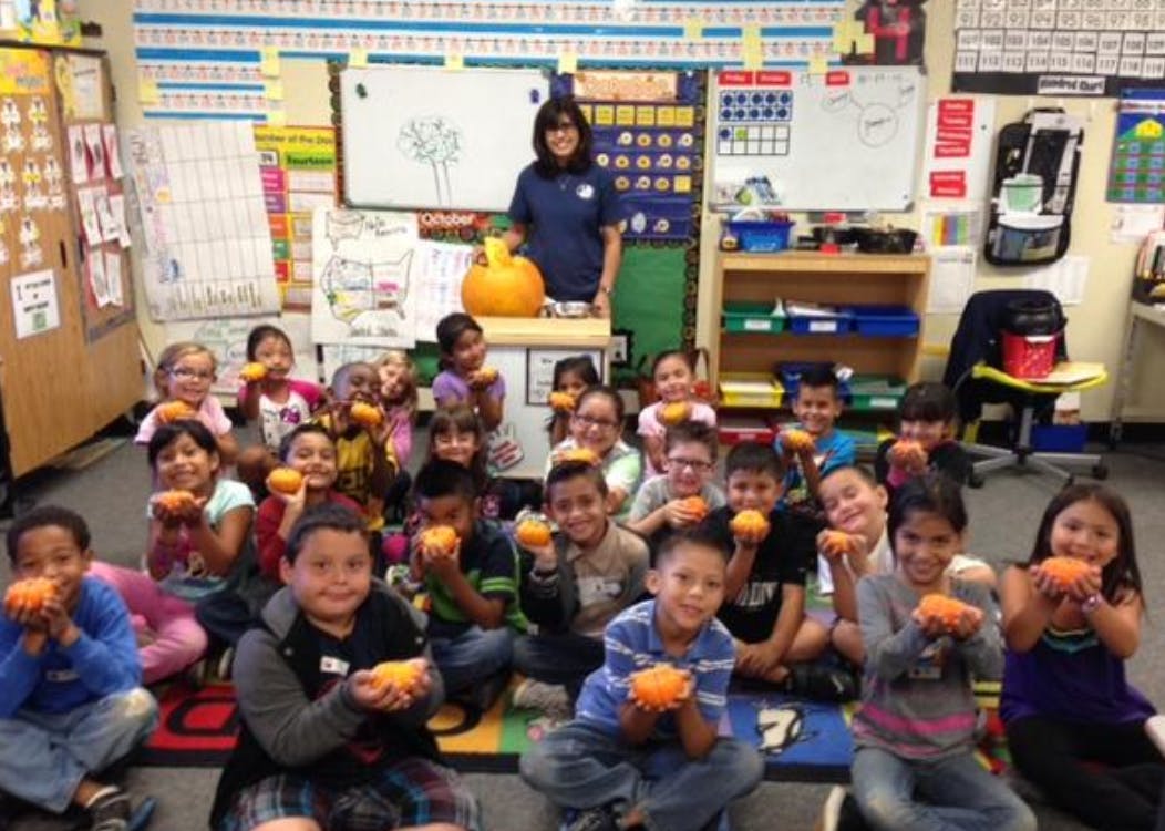 Adult and many children sitting on the floor holding small orange objects