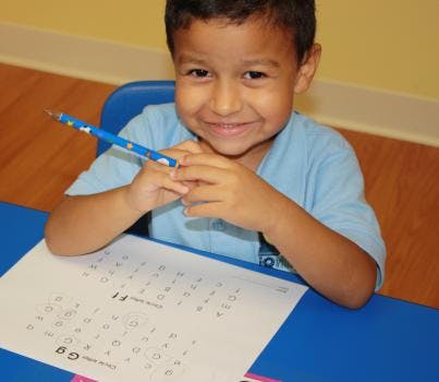 Child holding a pencil over a worksheet with letters