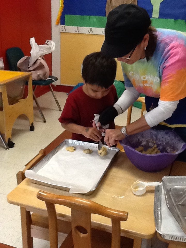 Adult and child scooping cookie dough onto a baking sheet in a classroom