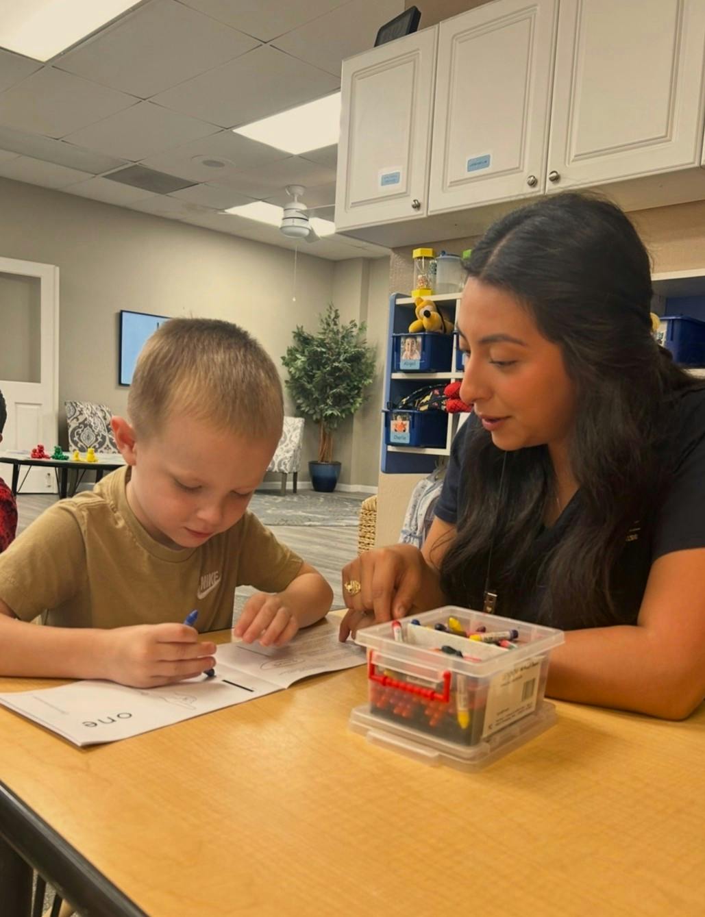 A person helping a child color in a worksheet in a classroom setting