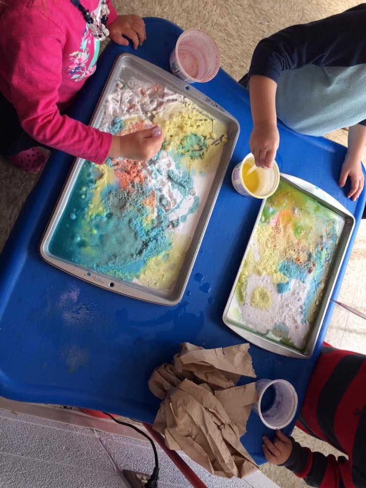 Two children playing with colorful sand and water in trays