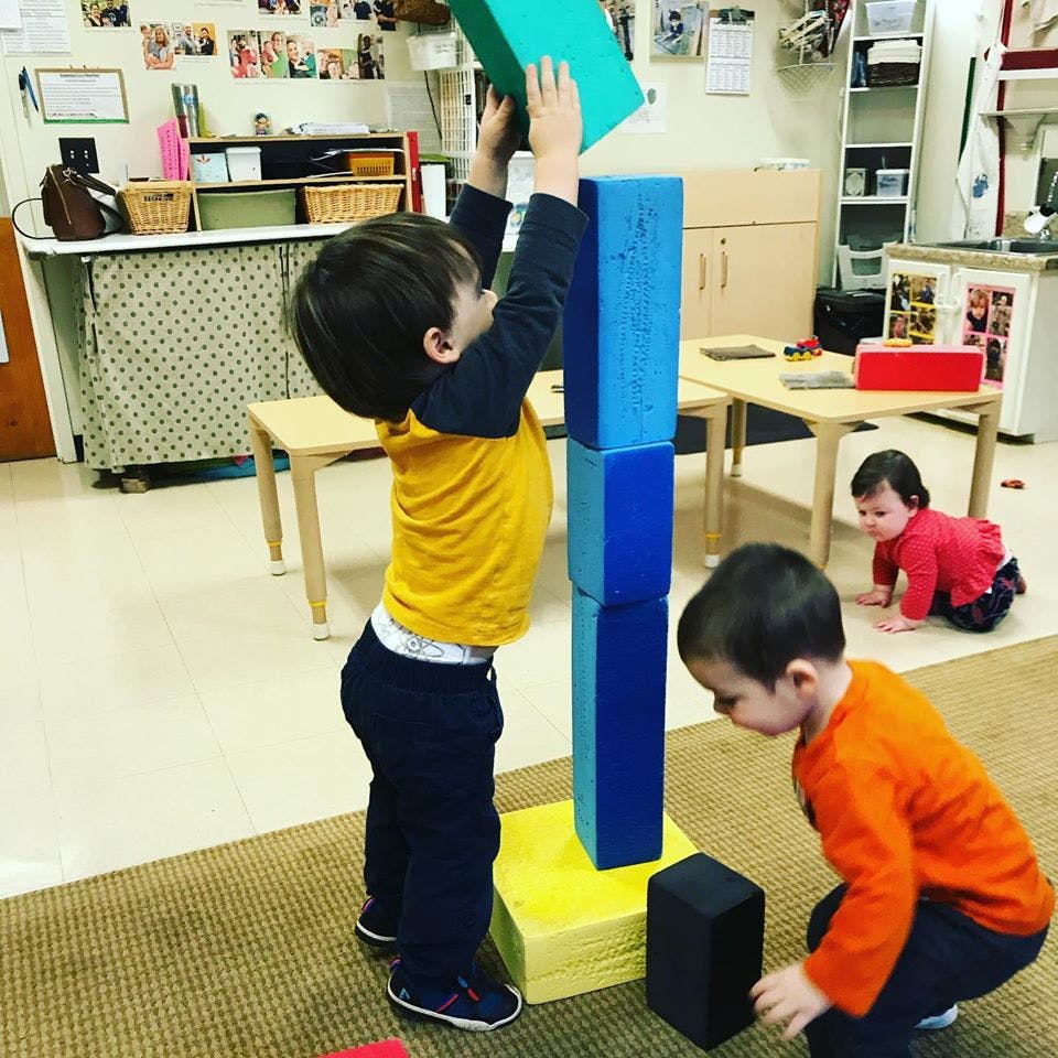 Child stacking large blocks in a classroom with other children