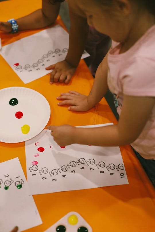 Child painting numbers on paper with red paint