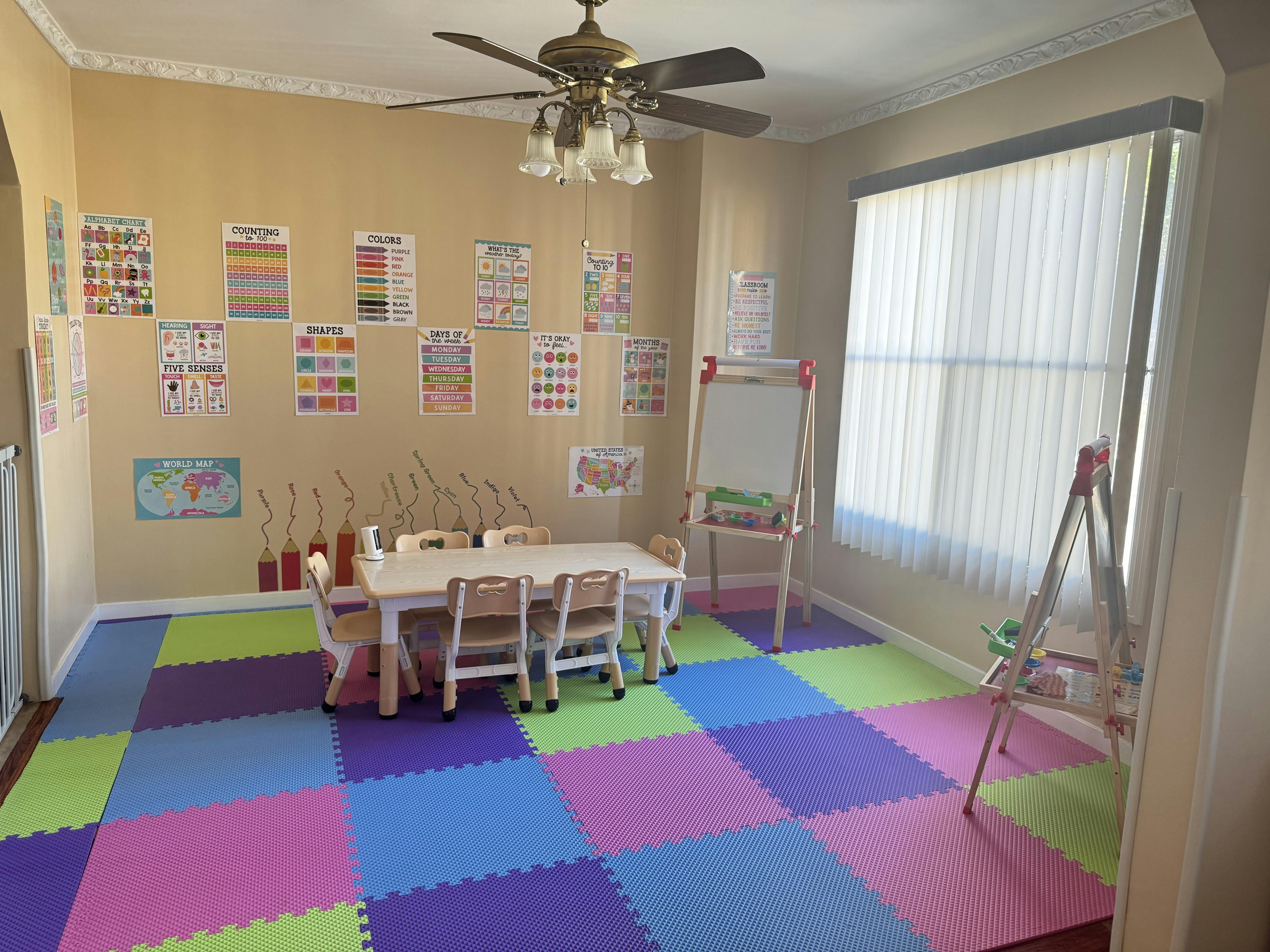Children's play area with colorful floor mats, small table and chairs, and wall charts