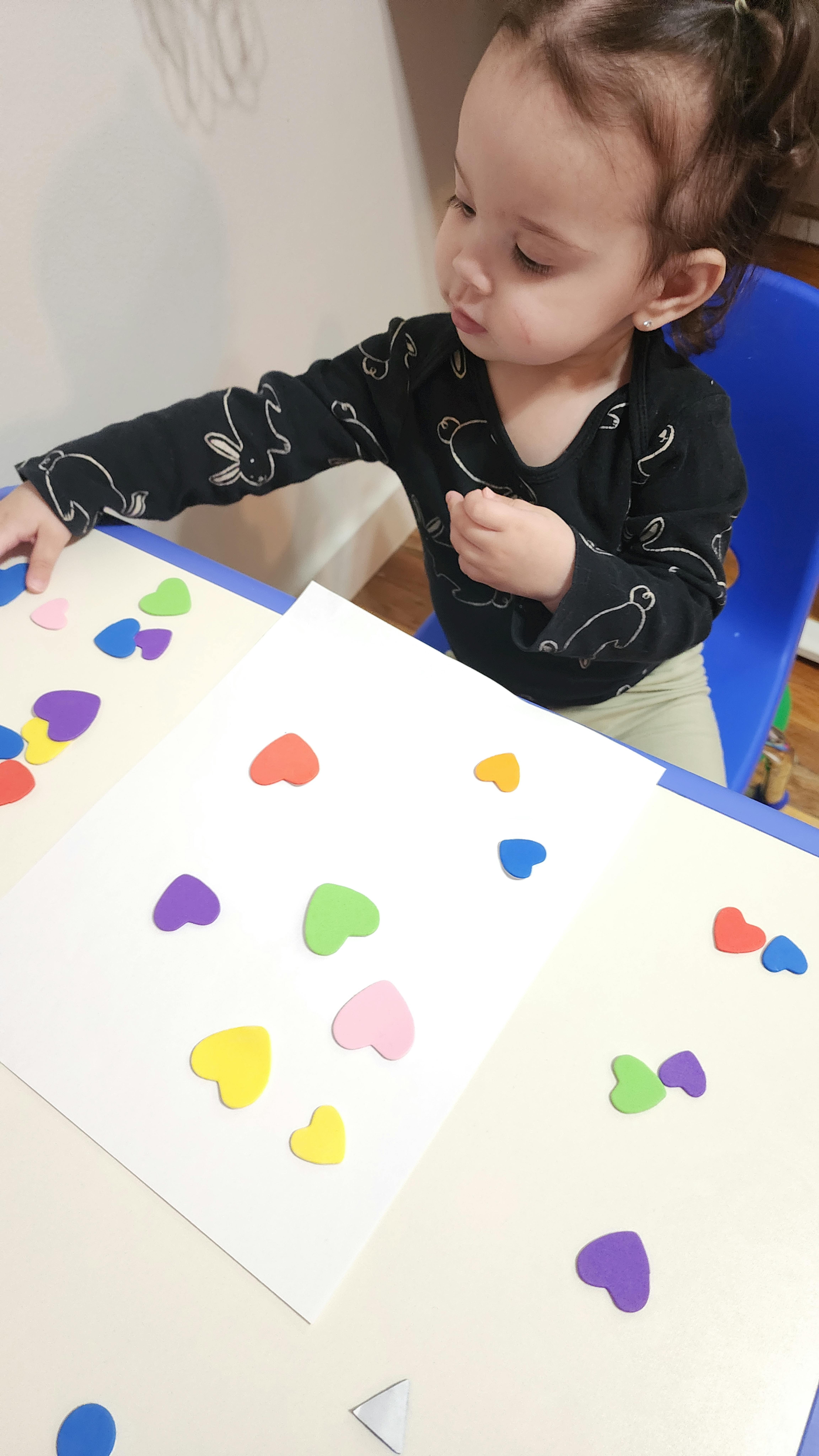 Child playing with colorful heart-shaped stickers on a table