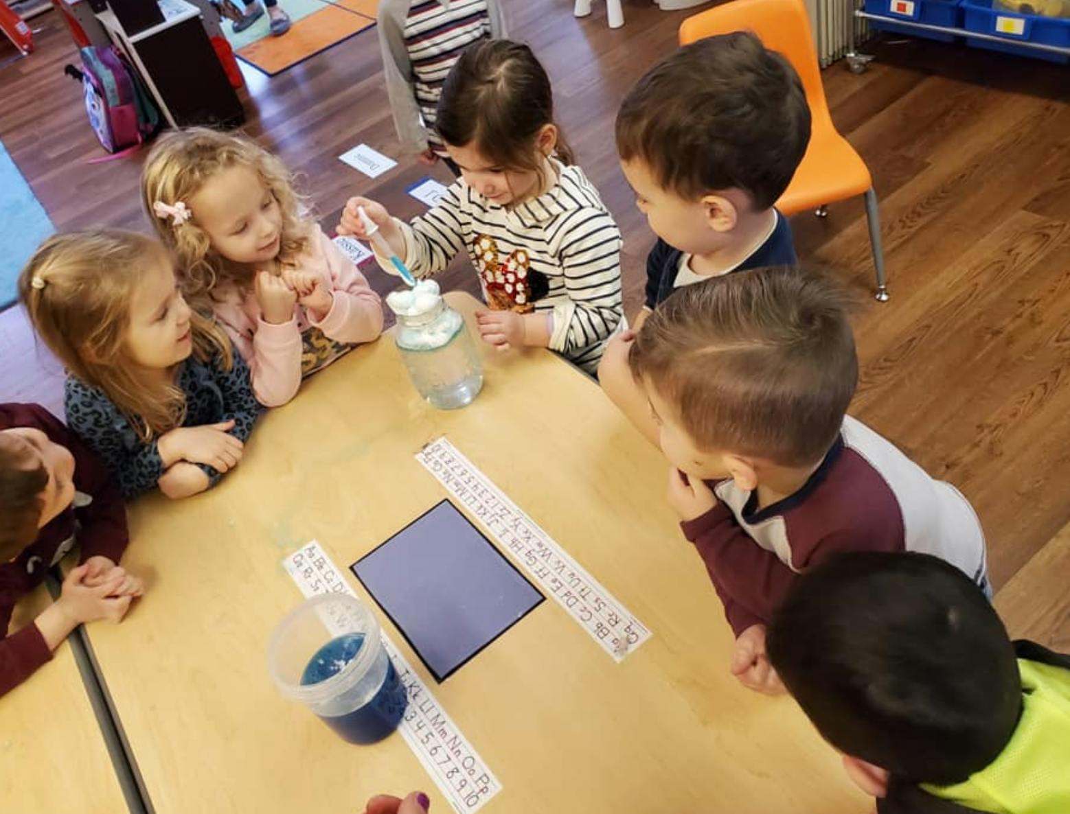Children gathered around a table, one child stirring a liquid in a jar