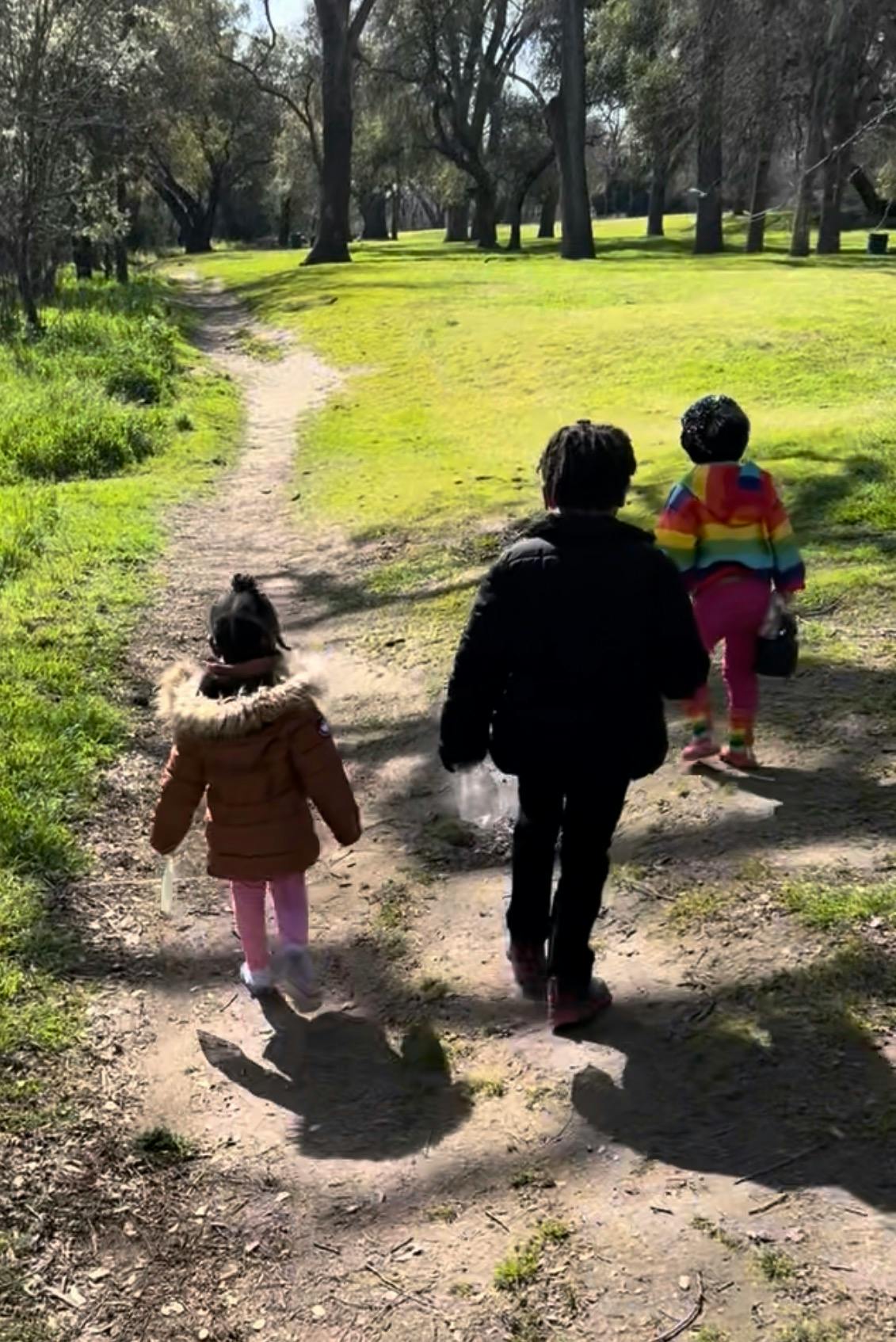 Three children walking on a dirt path in a park