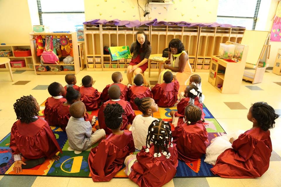 Two adults reading to a group of children in a classroom