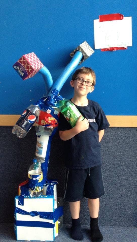 Child holding a plastic bottle next to a sculpture made of recycled materials