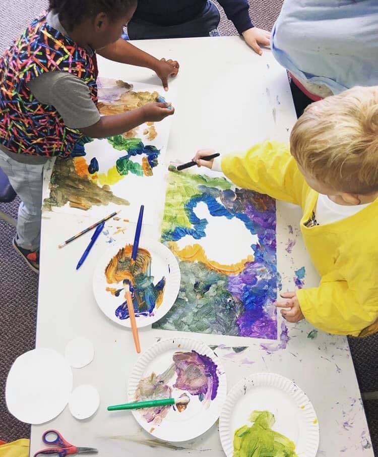 Two children painting on a large sheet of paper on a table
