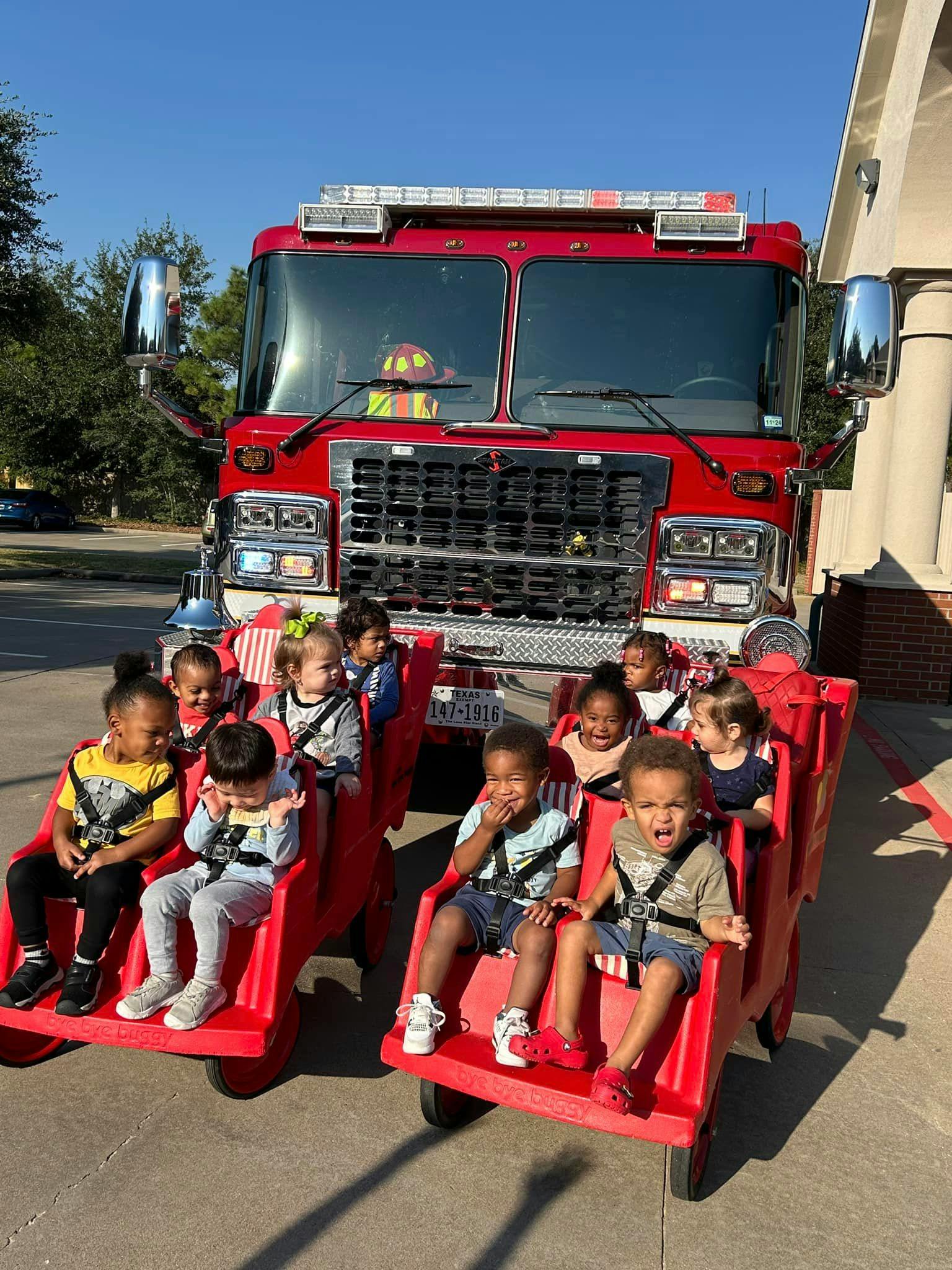 Children sitting in red wagons in front of a fire truck