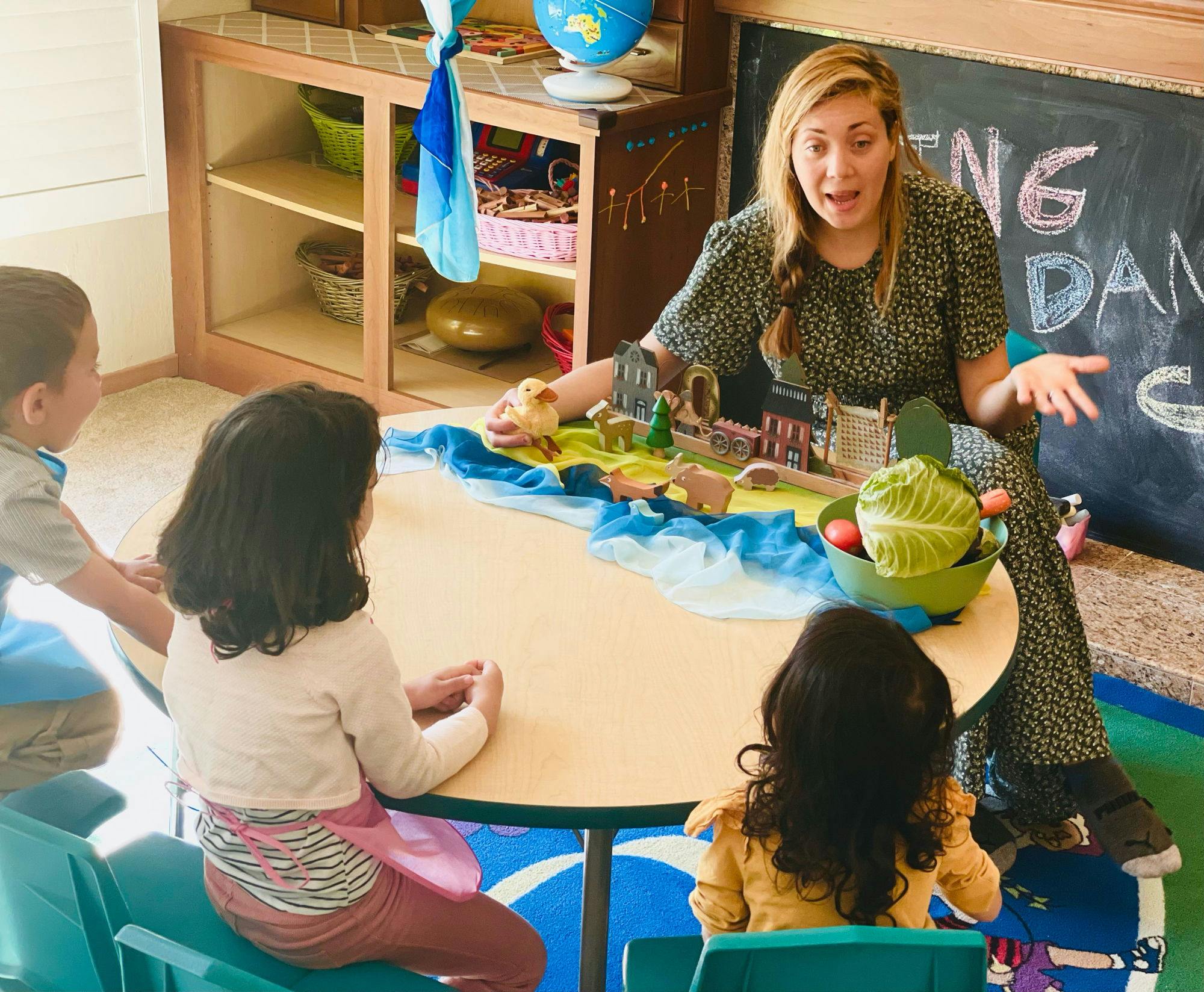 Person teaching children at a table with a diorama and vegetables